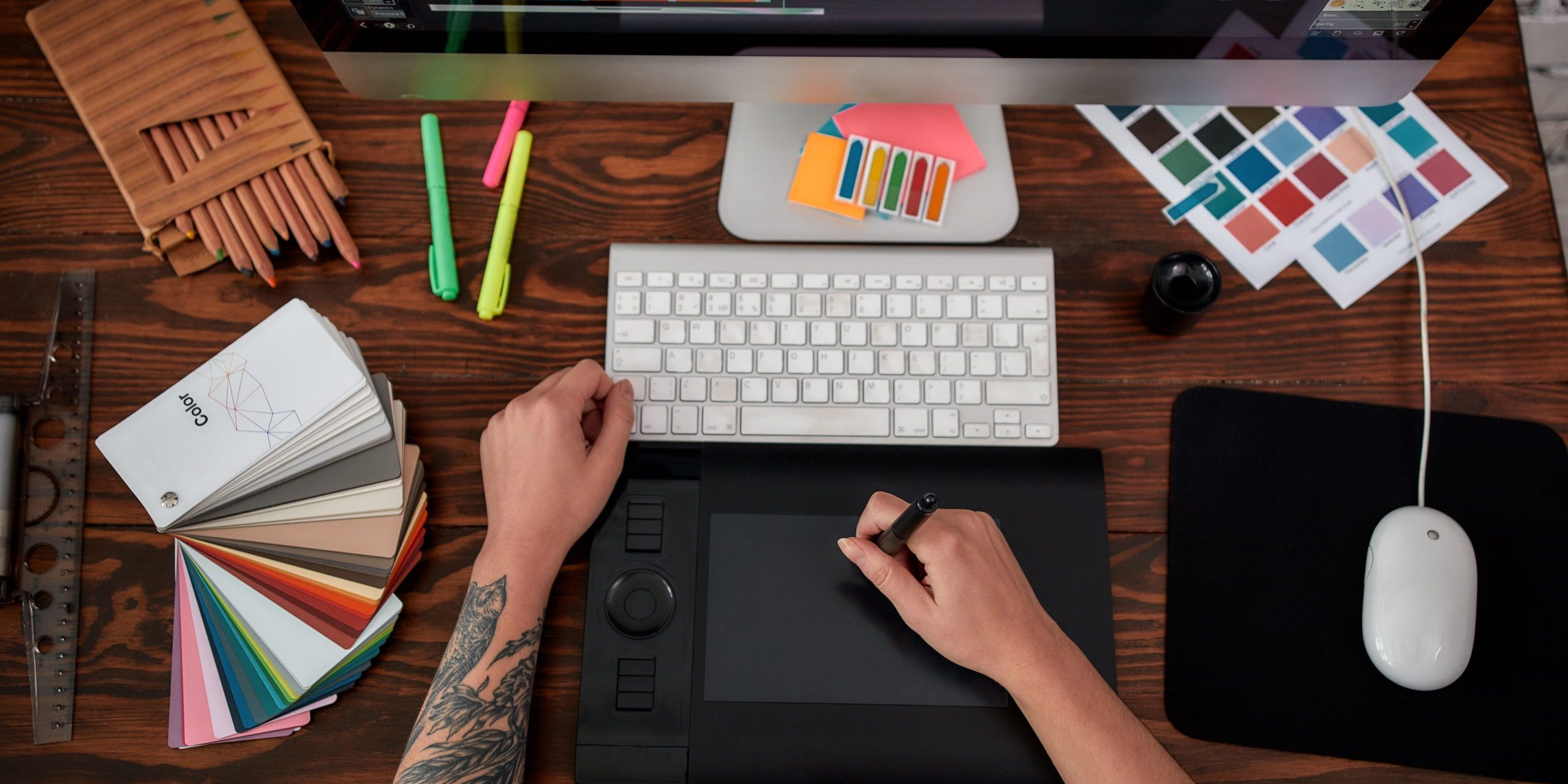 Professional web illustrator. Top view of a graphic designer using graphic tablet and computer in the office or studio. Workplace with graphic tablet, keyboard, computer and color swatches professional-web-illustrator.-top-view-of-a-graphic-designer-using-graphic-tablet-and-computer-in-the-office-or-studio.-workplace-with-graphic-tablet,-keyboard,-computer-and-color-swatches